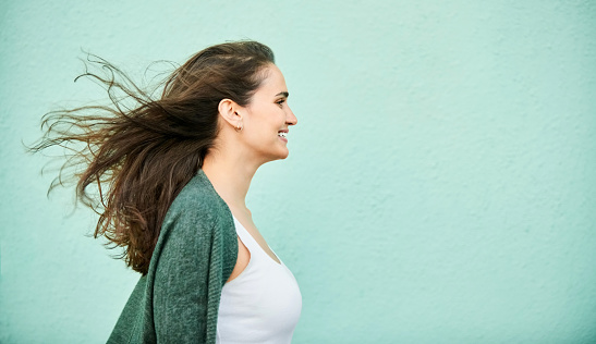 Profile shot of a beautiful young woman with her hairs flying against turquoise color wall