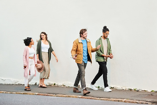 Full length of group of male and female friends walking against a white wall outside