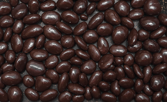Raisins or peanuts in chocolate, background of chocolate dragees close-up.