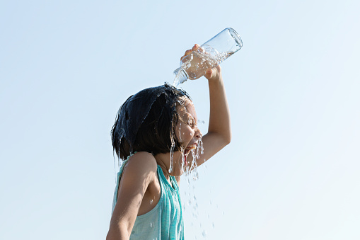 Little girl pouring water on her head using water bottle. She is trying to cool herself using cold water.