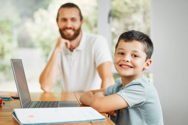 istock Learning, teaching and smiling little boy doing home school work online on a laptop. Happy son with caring father in the background ready to learn, study and have digital fun at the family house 1415870281
