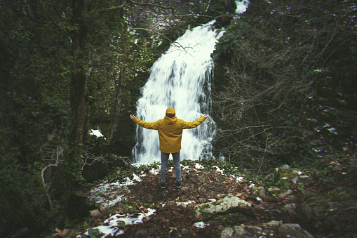 Portrait of a man arms raised with a yellow coat on a waterfall at Ayazma national park