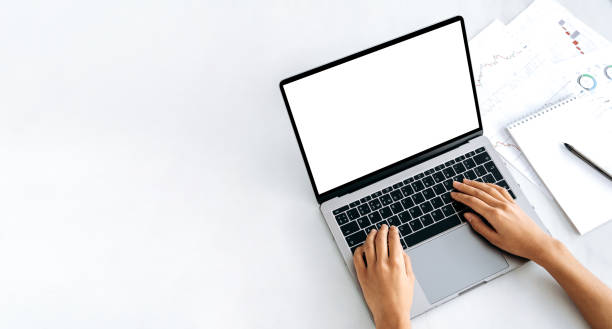 istock Copy space, mock-up concept. A laptop with a blank white screen, financial charts and a notepad lie nearby. Female hands on the keyboard, browsing the Internet, online correspondence 1415881690