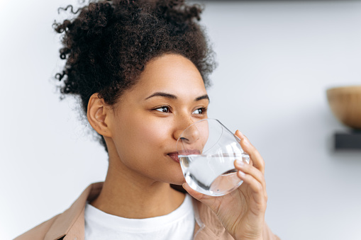 Healthy lifestyle concept. Pretty african american young woman drinks a glass of water at home. Lovely happy healthy mixed race girl follow healthy lifestyle, drink the daily amount of water