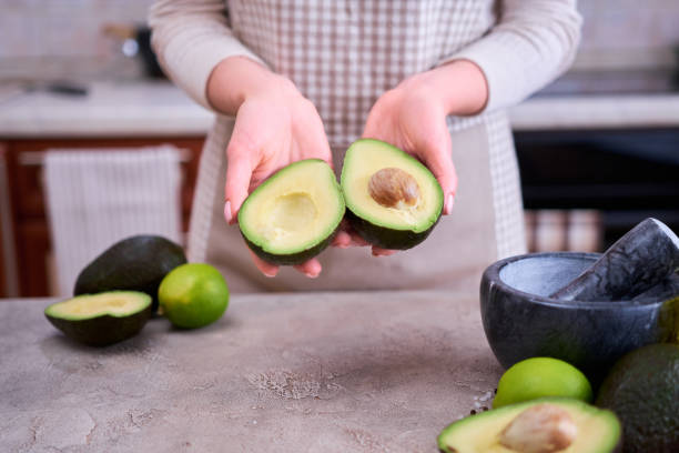 istock Closeup on hands holding fresh avocado cut in half over grey concrete table 1415888247