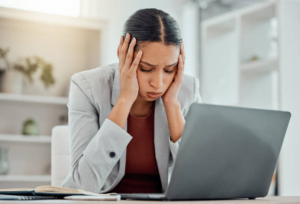Pain, headache and stressed finance manager feeling sick, tired and worried about a financial problem at her startup company. Young and frustrated professional businesswoman working at an office stock photo
