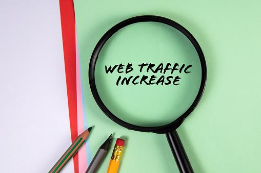 WEB TRAFFIC INCREASE. Magnifying glass on green paper background.