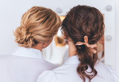 Two girls are friends. Rear view. They stand in front of the mirror in white clothes.