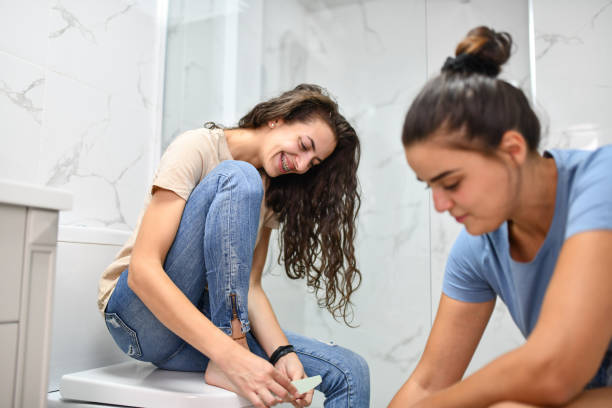 istock Smiling Female Cutting Toenails With Girlfriend In Bathroom 1415895540