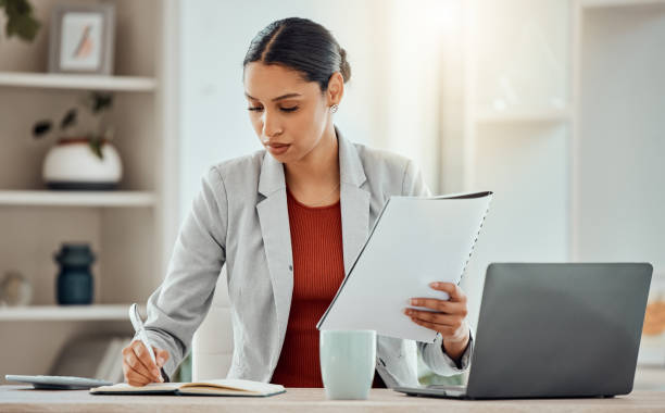 istock African Business woman planning, taking notes and writing in a notebook while reading a report, document or paperwork in an office alone at work. One serious corporate professional working at a desk 1415895598