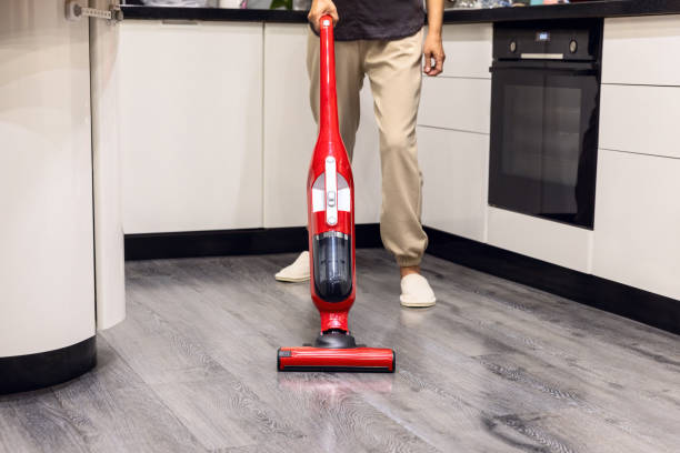 Mujer limpiando la cocina de una casa con una aspiradora roja. - foto de stock