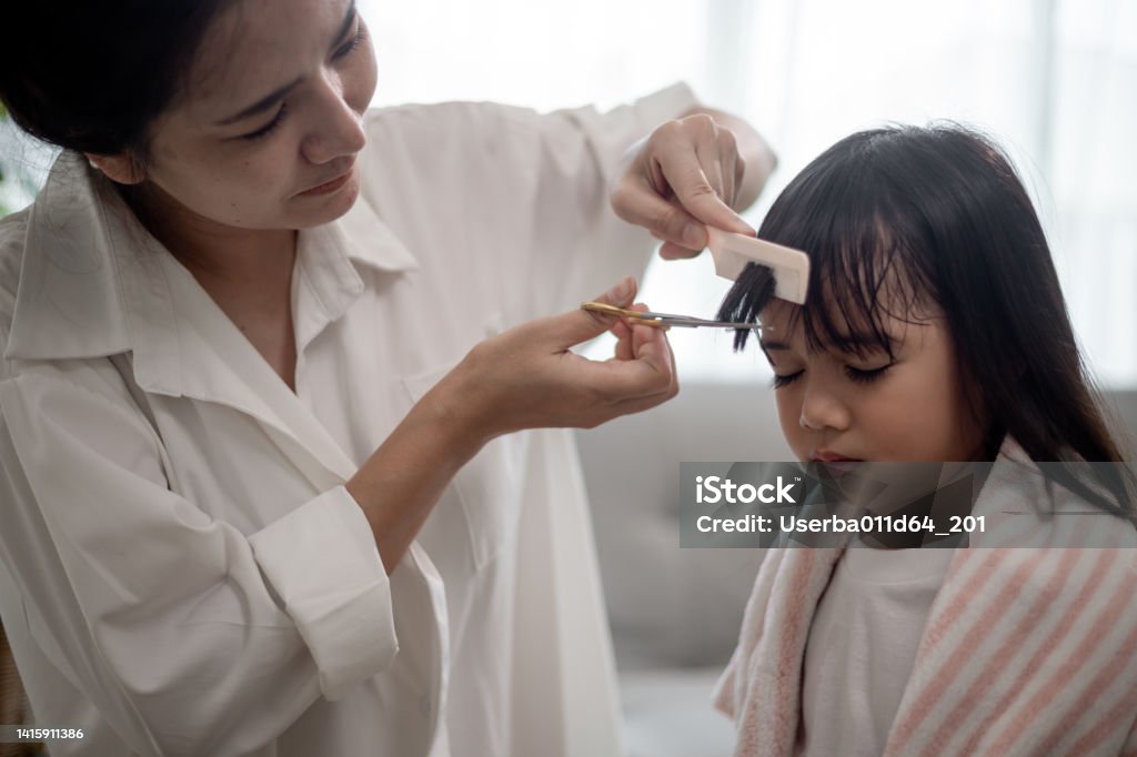 Asian Mother cutting hair to her daughter in living room at home while stay at home safe from Covid-19 Coronavirus during lockdown. Self-quarantine and social distancing concept. 35-39 Years Stock Photo