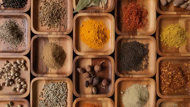 Many exotic, vibrant Indian food cooking spices in square wooden trays on display.