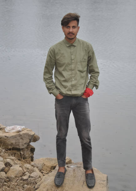 istock Full length of a young guy looking at camera, posing with hands in pocket while standing on stone by the lake 1415922213