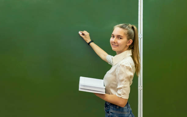 istock Beautiful teacher writing on the blackboard. Layout with space for text. 1415924319