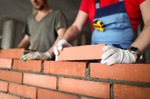 Close-up of builder laying brick with professional. Workmen at work, bricklayers building wall, contractor and worker. Masons using concrete and protective gloves