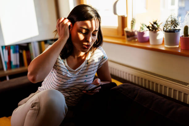 istock Young woman sitting on couch and using smartphone at home 1415929603