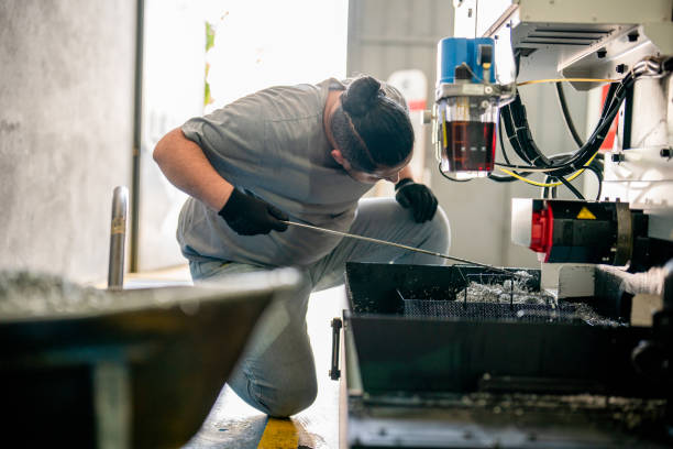 istock Blue collar worker cleaning CNC machine drill metal shavings 1415930253