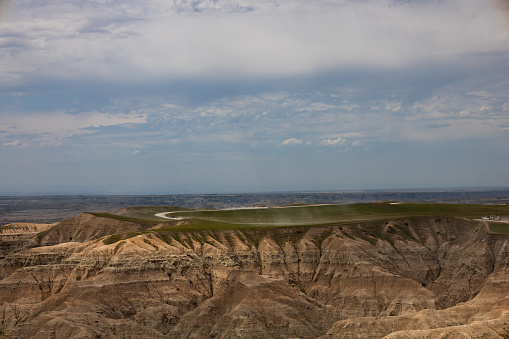 A picture taken at Badlands National Park, with a car driving and a trail of dust behind it