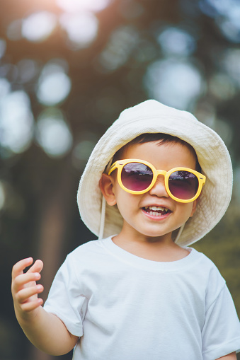 Portrait of Happy Asian little boy wearing hat and yellow sunglasses looking at camera outdoor