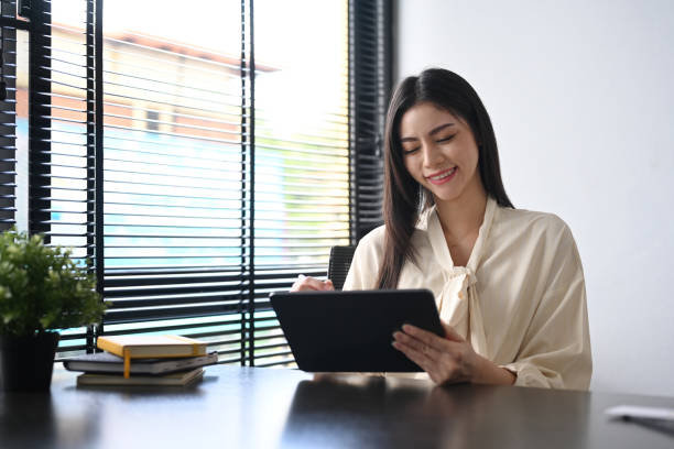istock Satisfied working woman sitting in contemporary office and using digital tablet. 1415938514