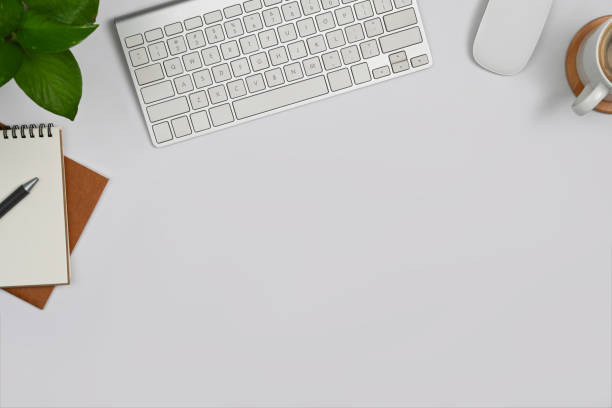 istock Simple workspace with blank notepads, coffee cup, wireless keyboard and houseplant on white table. 1415938527