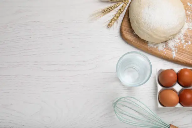 Flat lay composition with dough and ingredients on white wooden table, space for text. Sodawater bread recipe