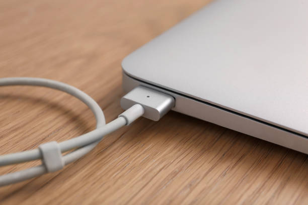 istock Modern laptop and charging cable on wooden table, closeup 1415950176