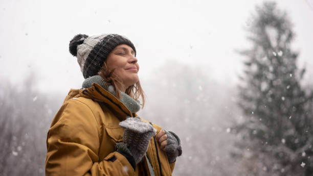 Young mature  adult caucasian woman in a hat and yellow jacket breathing fresh air in the winter forest stock photo