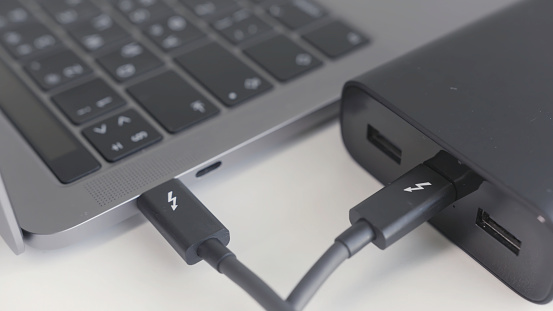 Black portable external power bank, for emergency device recharge. Close up of an open laptop is charged with a power bank via a cable, portable modern devices, external battery, cable, USB and laptop.