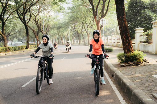 Two muslim  women riding bicycle in the city and the baby sitting on the back