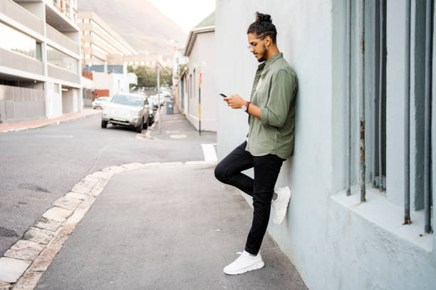 istock Young man leaning on a wall and texting on his phone 1415956423