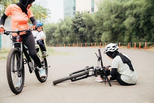 muslim woman  helping his friend to get up after falling from a bicycle.