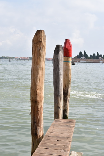 Three vertical wooden poles in the lagoon, the first painted red at the pointed end.