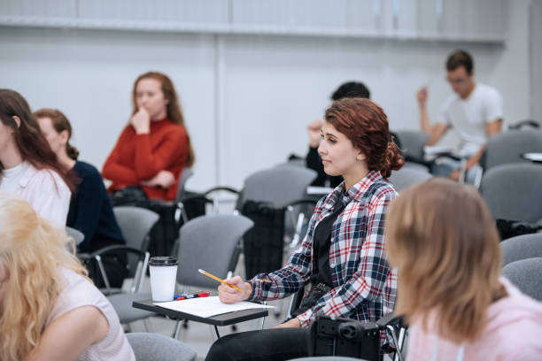Several university students in casual clothes are sitting in the audience for a lecture and listening to the teacher stock photo