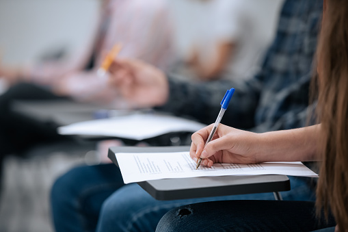 A close-up shot of a hand and a sheet of paper on which a student takes notes during a lecture at the university, without a face.