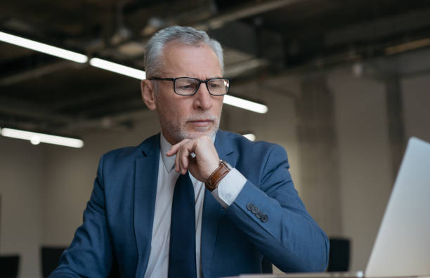 istock Senior businessman wearing glasses using laptop computer, planning project, brainstorming in modern office. Successful trader analyzing information, working online 1415964143