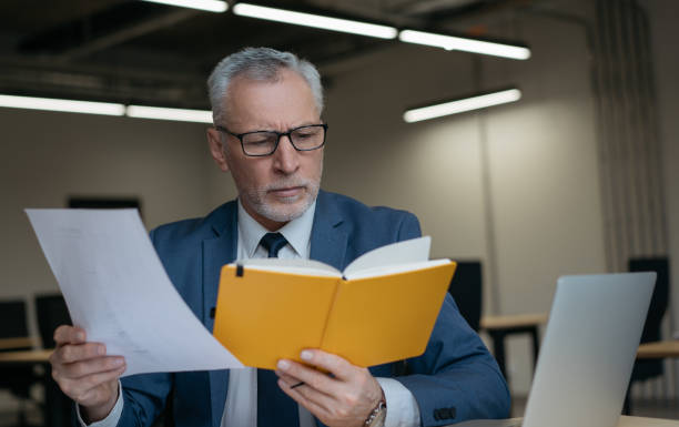 Senior businessman working in modern office. Portrait of successful banker holding financial report, analyzing documents at workplace stock photo