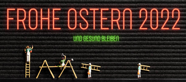 neon message in German for HAPPY EASTER 2022 - AND STAY HEALTHY and little painter figurines on a letter board background