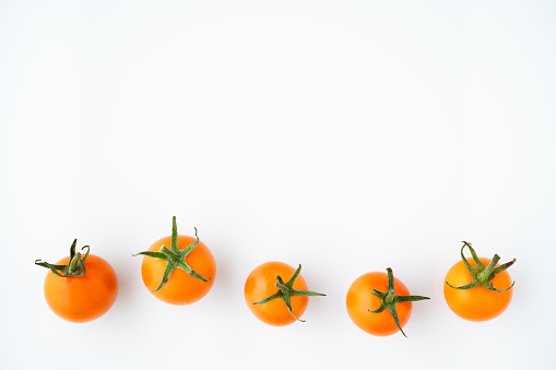 Fresh orange sungold cherry tomatoes in a row on a white background