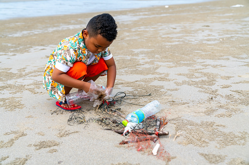 Happy African family on summer beach holiday travel vacation. Little boy picking up plastic bottle and garbage on the beach in sunny day . Environment protection volunteer and waste pollution concept.