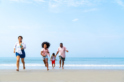 African family on beach holiday vacation. Father and mother with little daughter and son playing together on the beach at summer sunset. Parents with kid enjoy outdoor lifestyle together at the sea