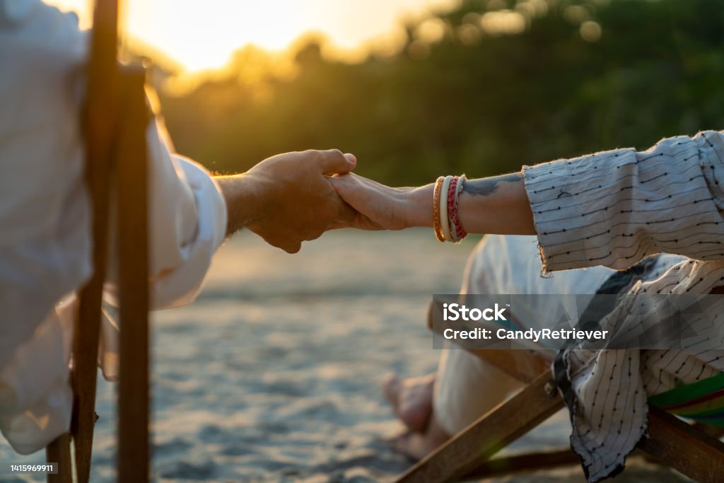 Asian senior couple relaxing together on the beach at summer sunset. Happy Asian family senior couple enjoy outdoor lifestyle on summer beach holiday vacation at the sea. Elderly retired man and woman relaxing on beach chair and holding hands together at summer sunset Holding Hands Stock Photo