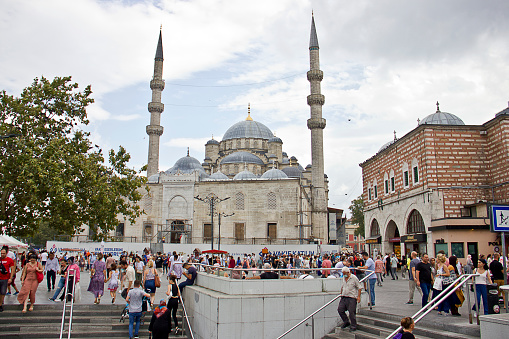 Istanbul,Turkey - August 10, 2022: People walking near the new Mosque or Yeni Cami in Istanbul, Turkey. There are also Mısır Çarşısı - Egyptian Spice Bazaar near the mosque. People pray, shopping and relaxing in this area.