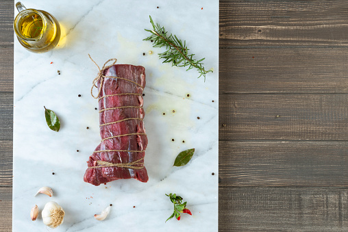 Directly above view of stringed beef on marble background on a rustic table with garlic, olive oil, pepper and rosemary.