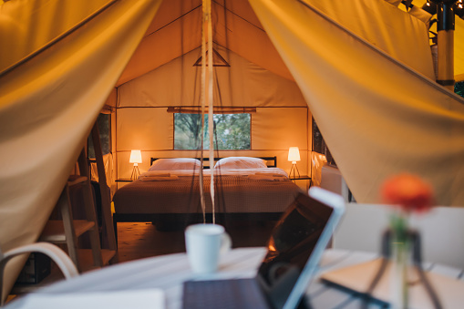 Interior of Cozy open glamping tent with light inside during dusk. Luxury camping tent for outdoor summer holiday and vacation. Lifestyle concept
