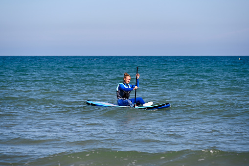 Erquy, France, July 8, 2022 - Young woman on a stand up paddle board (SUP) on the Atlantic beach of Erquy, Brittany