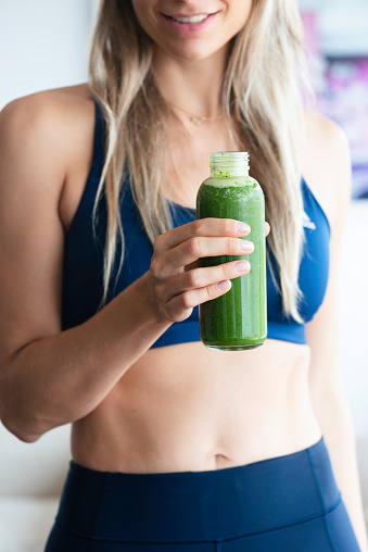 Woman is wearing dark blue sports clothing and is holding a green healthy drink in her hand.