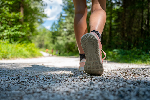Low angle view of a sole of a shoe of caucasian female walking or hiking on a path in the forest.