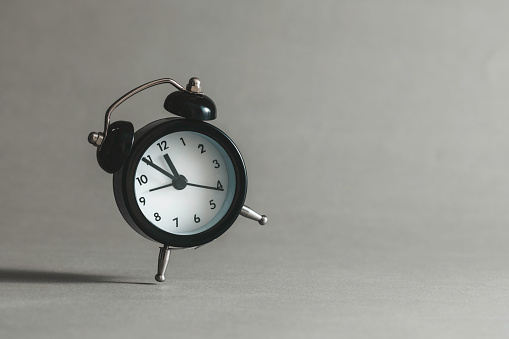 Black alarm clock  in front of gray  wall. The clocks time is showing 5 to 12.